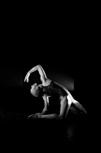 Solo dancer kneeling on floor arched backward with arm curved overhead.