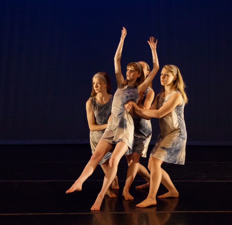 Three dancers support a solo dancer who is falling backwards. They look at something foreboding in the distance.