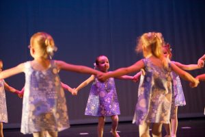 Pre-school children holding hands in a circle performing in ballet recital.