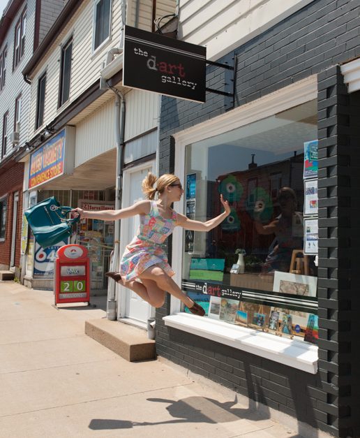 A humorous photo of a dancer jumping in front of "Kept", a downtown Dartmouth gift shop. she is looking into the window as if window shopping and excited about what she sees.