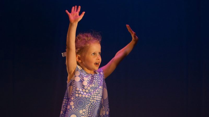 Young smiling child energetically throwing her arms overhead while dancing.
