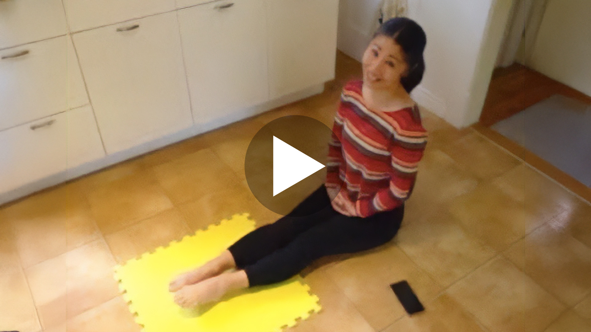 Dance instructor is sitting on the floor with her legs outstretched in front of her and hands folded in her lap. She is demonstrating foot exercises for dancers.