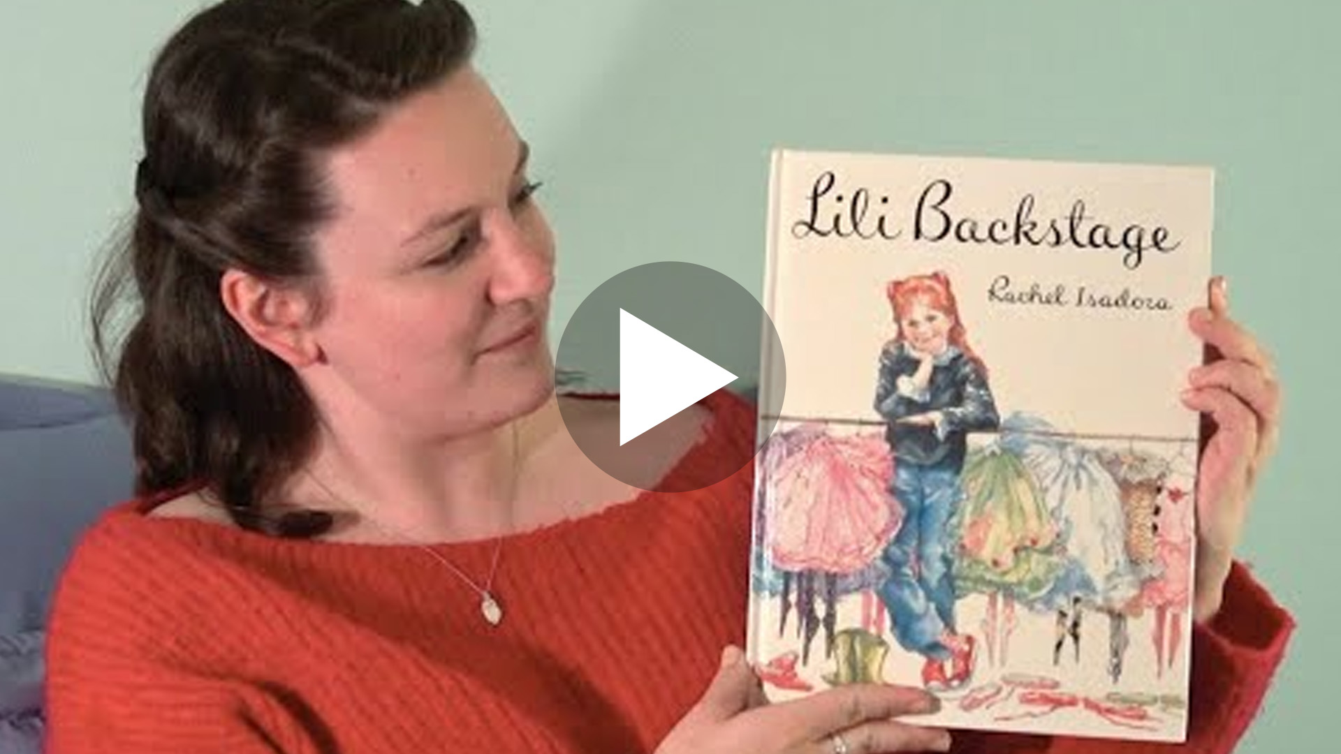 Photo of actor Rebecca Wolfe holding up book titled "Lili Backstage". The image is a link to the video of her reading to children.