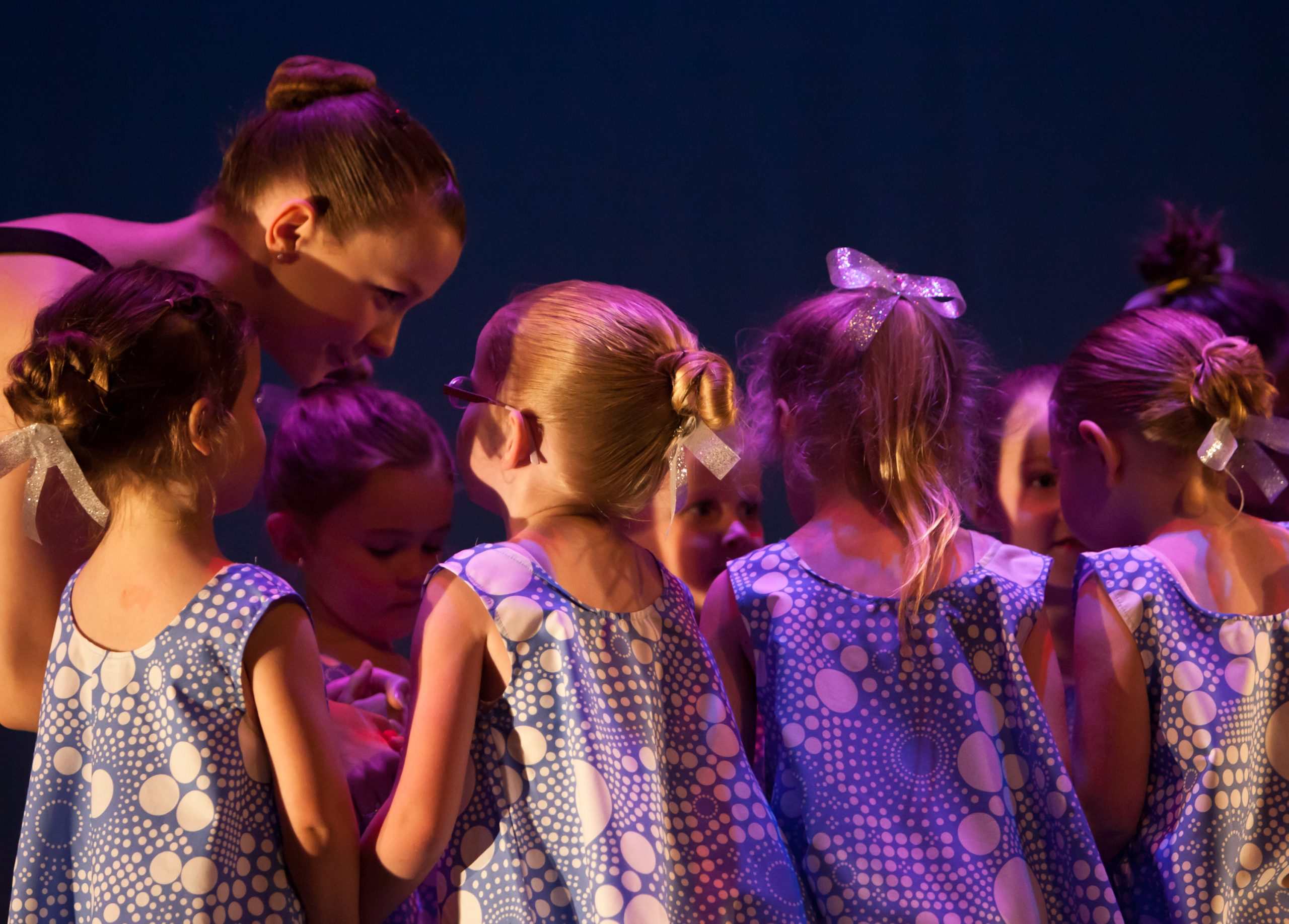 Teaching assistant guiding preschool dancers holding hands in a circle during recital at Leica Hardy School of Dance.